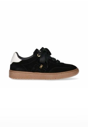 Sneaker in suede nera con un accento bianco sul tallone, suola in gomma testurizzata e lacci neri piatti. Presenta un design cucito e dettagli in hardware dorato.