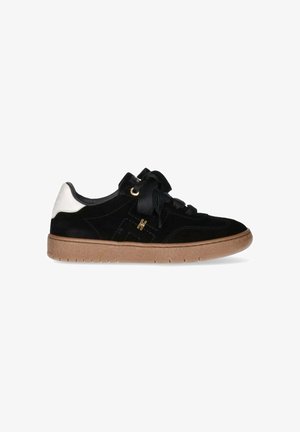 Sneaker in suede nera con un accento bianco sul tallone, suola in gomma testurizzata e lacci neri piatti. Presenta un design cucito e dettagli in hardware dorato.