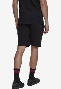 Shorts en coton noir à coupe décontractée, dotés d'une poche arrière. Portés avec des chaussettes noires à rayures rouges et vertes et des baskets noires.