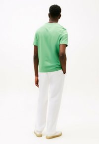 T-shirt verde a maniche corte in un tessuto morbido, abbinato a pantaloni bianchi. La maglietta presenta un colletto standard e una vestibilità comoda.
