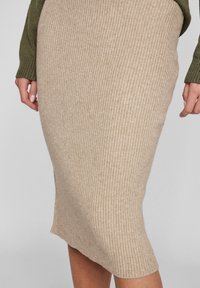 Beige ribbad stickad kjol med en åtsittande silhuett, med en midilängd och en subtil textur. Komplementerad av en olivgrön tröja på toppen.