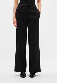 Melni plataji bikses ar gludu tekstūru, kas iezīmējas ar smalku punktiņu rakstu, priekšējiem kabatām un pielāgotu jostasvietu.