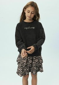 Sweatshirt gris foncé avec le texte "énergie magique", associé à une jupe en couches à rayures zébrées roses, mettant en avant une coupe décontractée et une texture douce.
