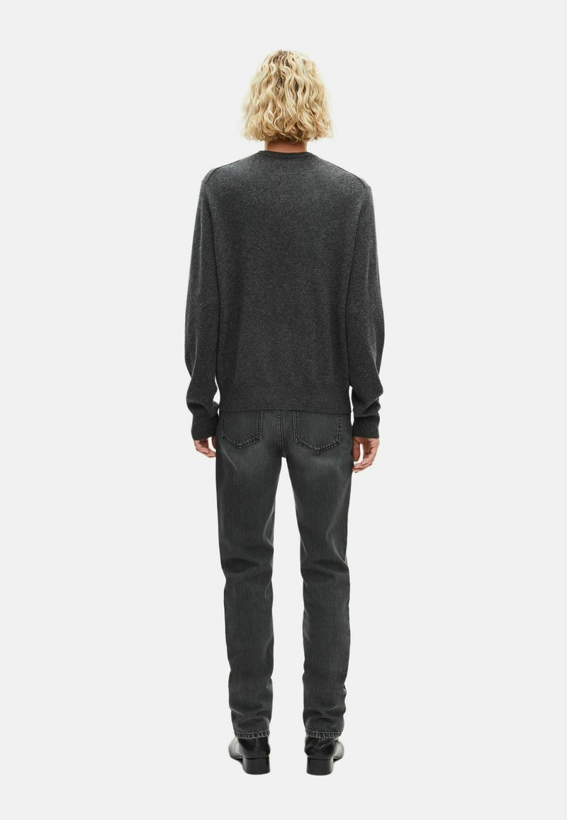 Grijze crewneck trui met lange mouwen, gecombineerd met donkergrijze jeans en zwarte enkellaarsjes, gezien vanachter tegen een witte achtergrond.