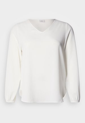 Blouse blanche à manches longues avec un col en V, confectionnée dans un tissu doux. Elle présente des poignets froncés et des fentes latérales, offrant une coupe décontractée et une texture lisse.