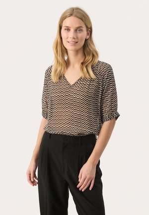 Bluse mit V-Ausschnitt aus semi-transparentem Material, mit einem Zickzackmuster in Braun und Creme, kombiniert mit hochgeschnittenen schwarzen Hosen.