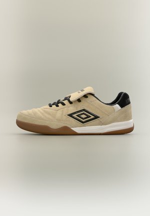 Chaussure de football d'intérieur en daim beige avec semelle en gomme, lacets noirs et logo Umbro sur le côté et sur la languette du talon.
