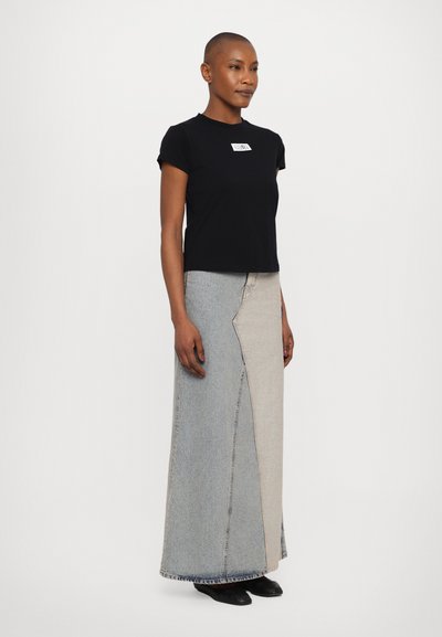 Black short-sleeve T-shirt with a white label and a long, multi-colored denim skirt featuring contrasting panel designs and a raw hem.