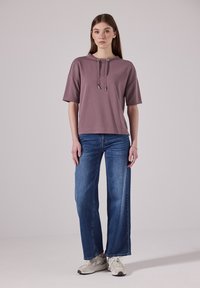Levandulová mikina s krátkým rukávem a šňůrkami, spárovaná s modrými širokými džíny a světlými teniskami. Hladká tkanina a uvolněný střih.