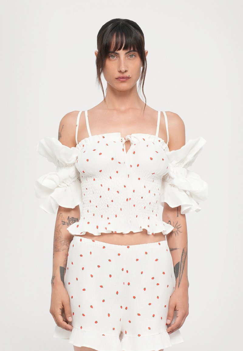Hvid bomuldsbluse med røde prikker, off-shoulder flæseærmer og snøre foran. Sammen med matchende shorts, som også har røde prikker.