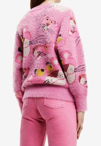 Pull en laine rose duveteux avec des motifs animaliers colorés, à coupe ample et bords côtelés. Assorti avec un pantalon en denim rose.