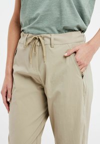 Šviesiai rudos spalvos lengvi kelnės su elastinga juosta ir šnioravimu, šoninėmis kišenėmis ir lygaus paviršiaus medžiaga. Sukurtos atsipalaidavusio silueto dizainu.