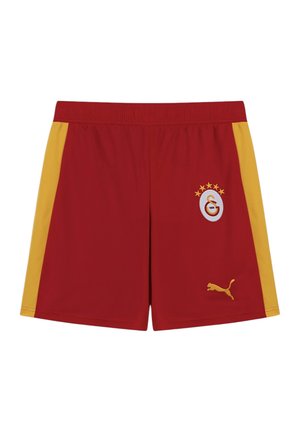 Shorts de sport rouges avec des bandes latérales jaunes, emblème de Galatasaray avec des étoiles sur la jambe droite, et logo Puma jaune sur la jambe gauche.