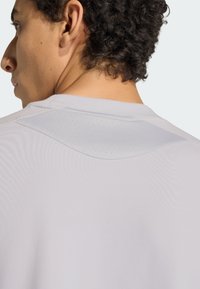 Szary sportowy T-shirt z teksturowanym kołnierzem, z przewiewnymi perforacjami w okolicy pleców. Gładka tkanina i dopasowany krój.