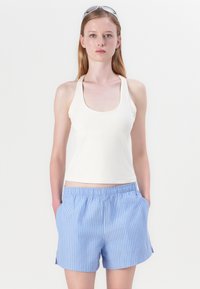 Witte tanktop met brede banden, gecombineerd met blauw-witte gestreepte shorts. De shorts hebben een elastische tailleband en zijzakken.