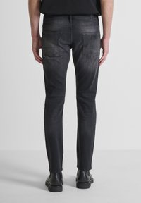 Vaqueros de denim negro con un corte ajustado, que presentan una sutil textura desgastada, dos bolsillos traseros y un pasador para cinturón, combinados con botas negras.