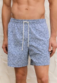 Pantaloni da bagno con motivo blu, dotati di cintura elastica e cordino regolabile. Design geometrico in blu chiaro e scuro su un tessuto morbido.