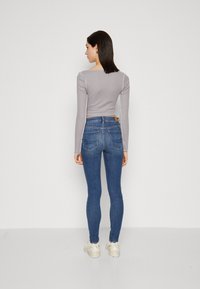 Fittet grå langermet topp og blå smale jeans. Toppen har firkantet utringning; jeansene har baklommer med sømdetaljer.