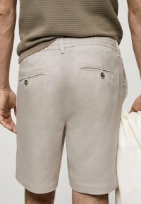 Shorts gris clair en tissu lisse, dotés de deux poches arrière avec des boutons décoratifs et d'une taille élastique.