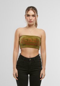 Olijfgroen, strapless cropped top met het "Von Dutch Originals" logo in oranje strass-steentjes. Draagt een hoge taille zwarte spijkerbroek.