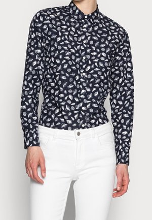 Chemise bleu marine à boutons avec un motif de coquillage blanc, à manches longues et col standard. Assortie à un pantalon blanc. Le tissu semble lisse et léger.