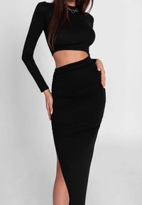 Musta pitkähihoinen crop-top, yhdistettynä korkea vyötäröiseen mustaan hameeseen, jossa on sivuavastus ja kerätty rakenne. Silkkinen kangasviimeistely.