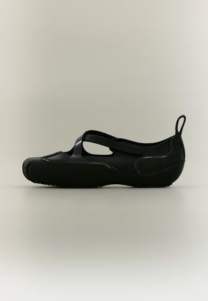 Scarpa piatta nera con punta chiusa, ritaglio sul lato, cinturino sul collo del piede e linguetta sul tallone.