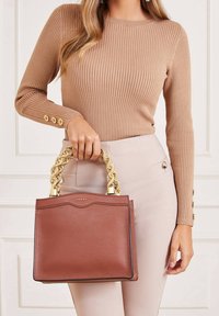 Sac à main en cuir marron texturé avec une anse tressée couleur or et un logo subtil, présentant une forme rectangulaire et des bords noirs contrastants.