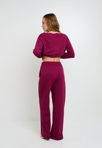 Top court fuchsia à manches longues avec une découpe dans le dos, associé à un pantalon large assorti. Texture douce avec un léger effet de brillance.
