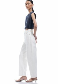 Marineblauw en witte gestreepte cropped top met knopen, gecombineerd met hoge witte wijde jeans. Model draagt witte spandalen met bandjes.