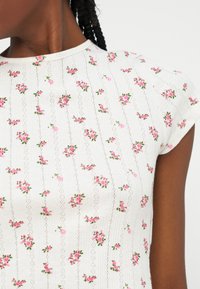 Εγκαρσίος πλάνος ενός ατόμου που φοράει λευκή πλεκτή μπλούζα με μικρά ροζ λουλουδένια μοτίβα και κοντά μανίκια.