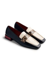 Mocassins en cuir noir avec un bout carré, ornés d'une sangle crème à motif serpent et d'un petit talon bloc rouge. Texture lisse dans l'ensemble.