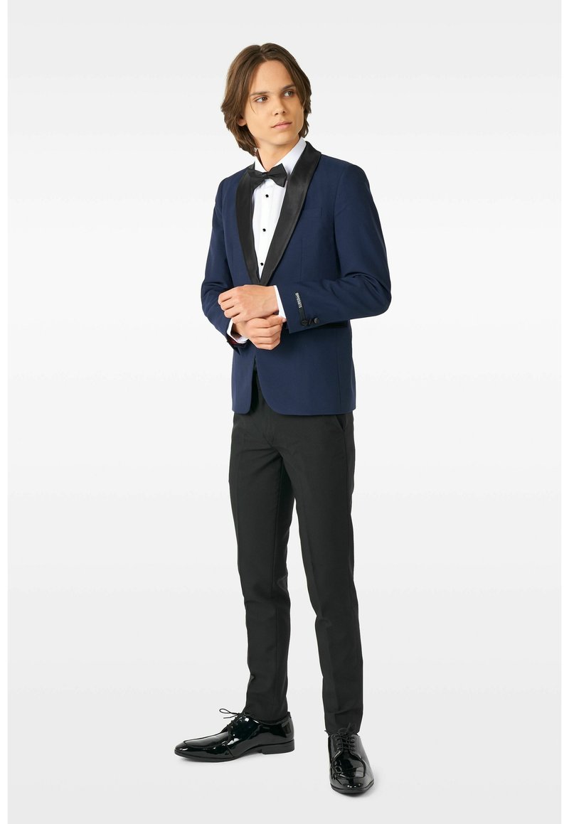 Marineblauer Smokingjacke mit Satinrevers, schwarze Hose und glänzende schwarze Schuhe. Weißes Hemd mit einer schwarzen Fliege. Slim-Fit-Design.