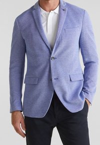 Blue textured blazer with a tailored fit, single button closure, notch lapels, and two front pockets. Worn over a white polo shirt.
