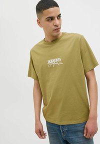 Olivza zaļas kokvilnas T-krekls ar apaļu kaklu un īsām piedurknēm; uz krūtīm ir balts "Jack & Jones" logo kursīvā.