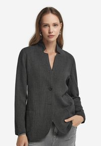 Szary blazer z teksturowanej tkaniny, z kołnierzem typu stójka, zapięciem na jeden guzik i dwiema przednimi kieszeniami. Posiada dopasowany krój i gładką tkaninę.