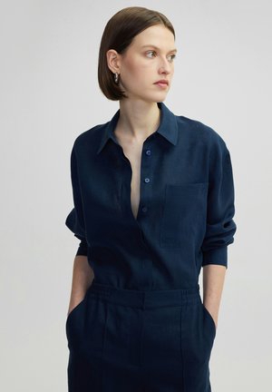 Marineblauwe linnen shirt met kraag, lange mouwen, een borstzak en knoopsluitingen. Zachte textuur met een relaxte pasvorm.