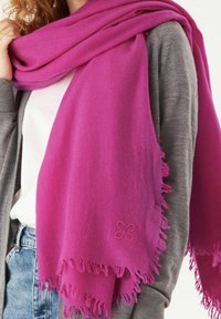 Écharpe rose en matériau doux, avec un bord frangé et un petit détail de broderie en forme de fleur. Portée drapée sur un pullover gris.