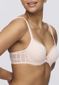 Light pink bra with lace trim and textured side panels; features smooth cups and adjustable straps, displaying a delicate design.