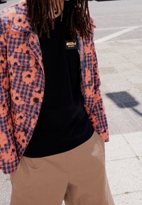 Pink and blue patterned blazer over a black t-shirt with "Moschino" label; beige pants. Textured fabric with a checkered design.