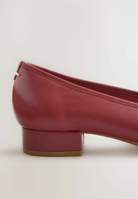 Bailarina de cuero rojo con un tacón bajo y cuadrado. Presenta una textura suave y un pequeño detalle dorado cerca de la parte trasera del zapato.