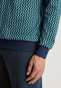 Patroon sweatshirt met marineblauwe boorden en onderrand; geometrische vormen in tinten van groenblauw en wit op een donkere achtergrond; zachte stofstructuur.