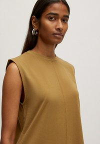 Beige ärmelloses Oberteil mit Rundhalsausschnitt, glatter Textur und leichtem Glanz. Verfügt über dezente Nähte entlang des vorderen Panels.