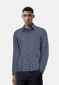 Camicia a maniche lunghe di colore blu navy con piccolo motivo floreale bianco, con colletto e chiusura a bottoni, realizzata in tessuto morbido, indossata con pantaloni scuri.