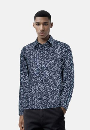Camicia a maniche lunghe di colore blu navy con piccolo motivo floreale bianco, con colletto e chiusura a bottoni, realizzata in tessuto morbido, indossata con pantaloni scuri.