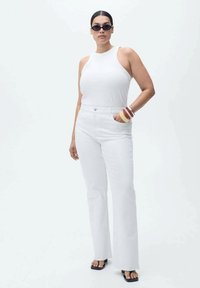 Top alb fără mâneci asortat cu blugi albi evazați. Accesorii includ ochelari de soare și brățări suprapuse. Textură fină, design minimalist.