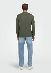 Chemise verte à manches longues avec un col rond, associée à un jean ample bleu clair et des baskets blanches, vue de dos.
