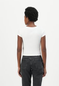 White ribbed crop top with short sleeves, paired with dark grey jeans featuring back pockets and a straight-leg design.