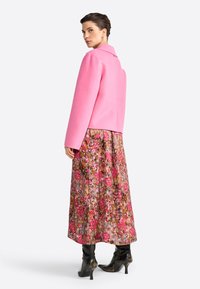 Chaqueta de mezcla de lana rosa con cuello entallado, combinada con una falda larga de estampado floral en tonos rosa y marrón, llevada con botas de tacón negras.