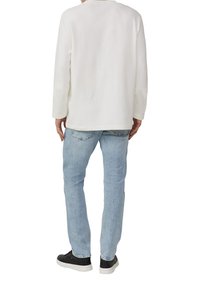 Weißes Langarmshirt mit Rundhalsausschnitt, kombiniert mit hellblauen Jeans und schwarzen Turnschuhen, von hinten betrachtet.